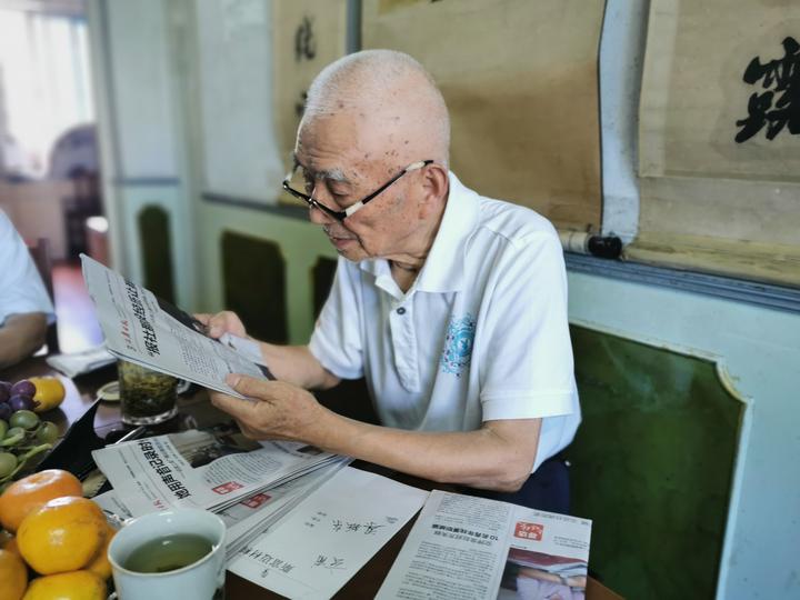 (樊吉昌戴着老花镜在阅读本报寻访老媒体人栏目上的文章